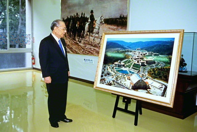 画像・イーゼルに立てかけられた縦１メートル、横２メートルほどの金縁の額にはいったアメリカ創価大学の写真の横に立ち、写真を見下ろしている池田先生